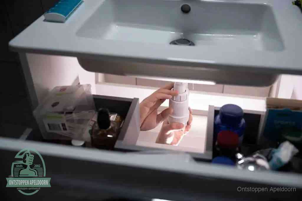 Een pompfles met zeep boven een wastafel, de heet water en afwasmiddel-methode om een vetprop in de afvoer los te maken in Apeldoorn