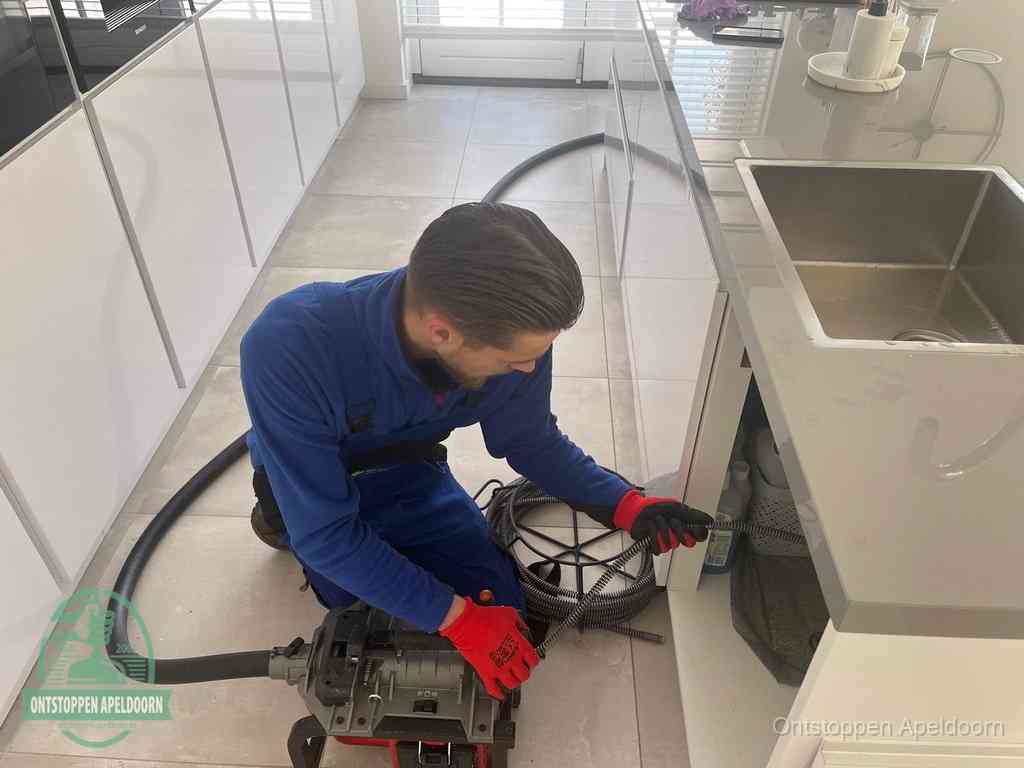 Een monteur ontstopt de keukenafvoer onder de spoelbak met een elektrische veermachine in Apeldoorn