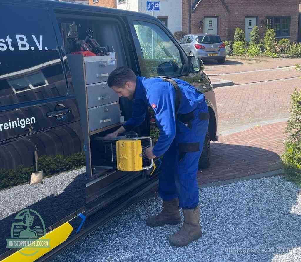 Een monteur pakt buiten op de oprit gereedschap uit de bedrijfsbus, het moment om een professional in te schakelen voor een verstopte afvoer in Apeldoorn
