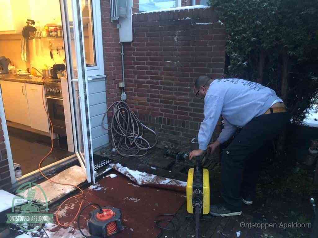 Een monteur werkt buiten bij een open riool-/grondput met een elektrische ontstoppingsmachine om een verborgen afvoerprobleem op te sporen in Apeldoorn