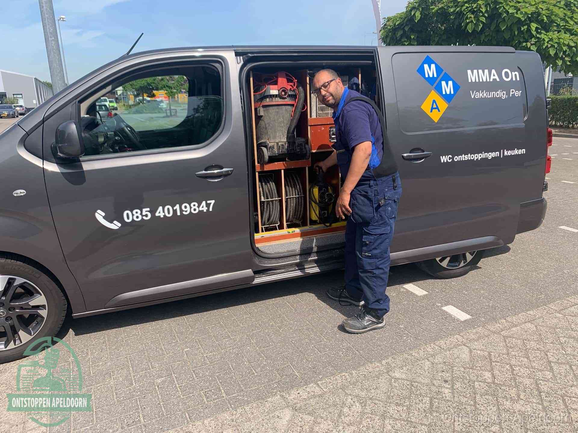 Een monteur bij de open schuifdeur van zijn bedrijfsbus op een parkeerplaats, klaar om de oorzaak van terugkerende afvoerverstoppingen aan te pakken in Apeldoorn