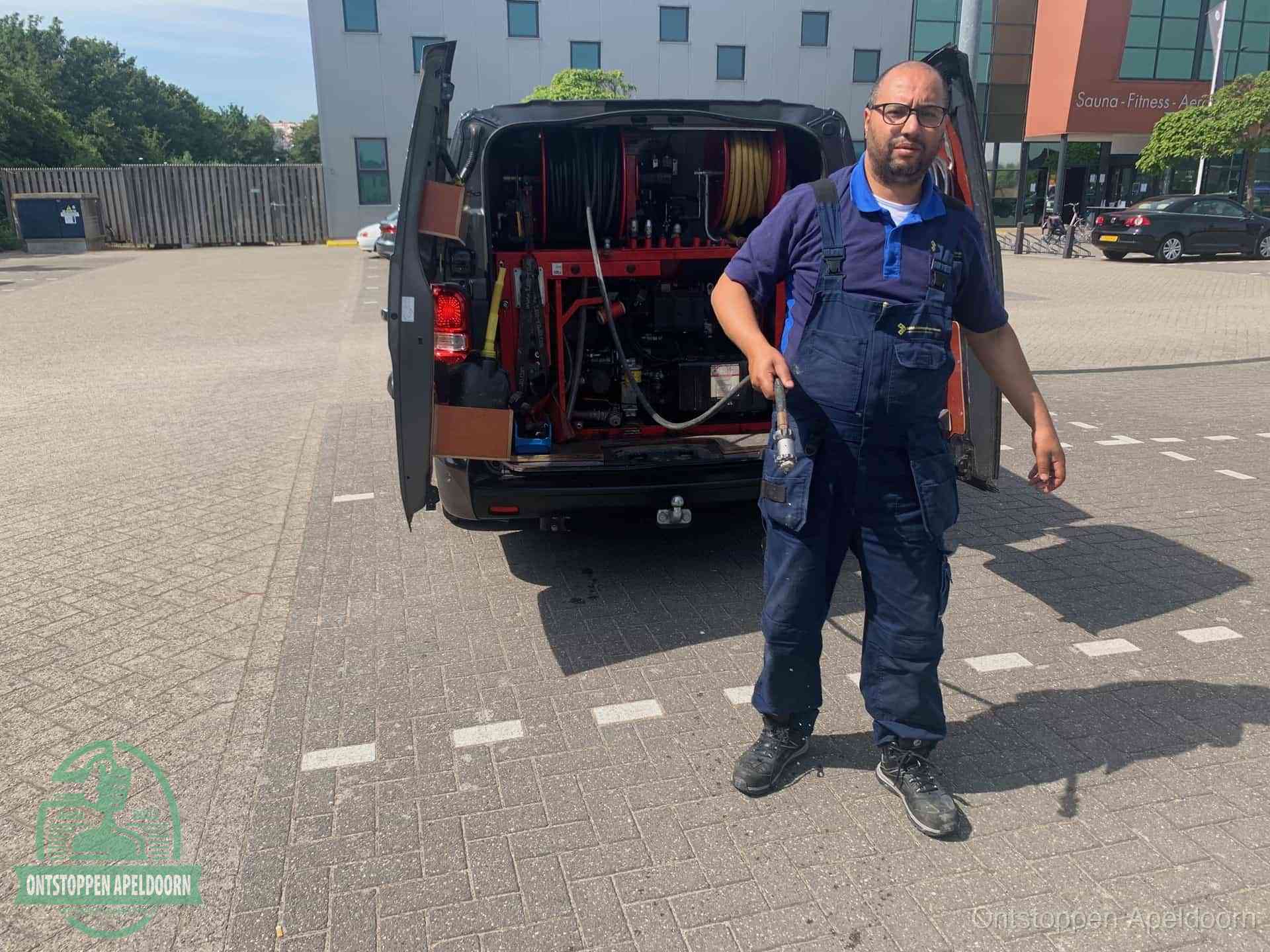 Een monteur bij zijn bestelbus met een hogedruk- en rioolreinigingsunit, klaar om de oorzaak van terugkerende wc-verstoppingen aan te pakken in Apeldoorn