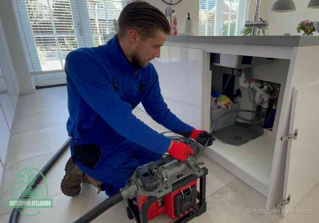 Een monteur voert een professionele elektrische ontstoppingsmachine in de afvoer onder de spoelbak tijdens het gootsteen ontstoppen in Apeldoorn