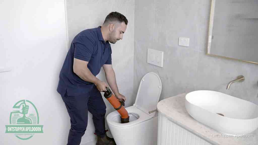 Een man gebruikt een handmatige luchtdruk-ontstopper in een modern betegeld toilet om zelf de wc te ontstoppen in Apeldoorn